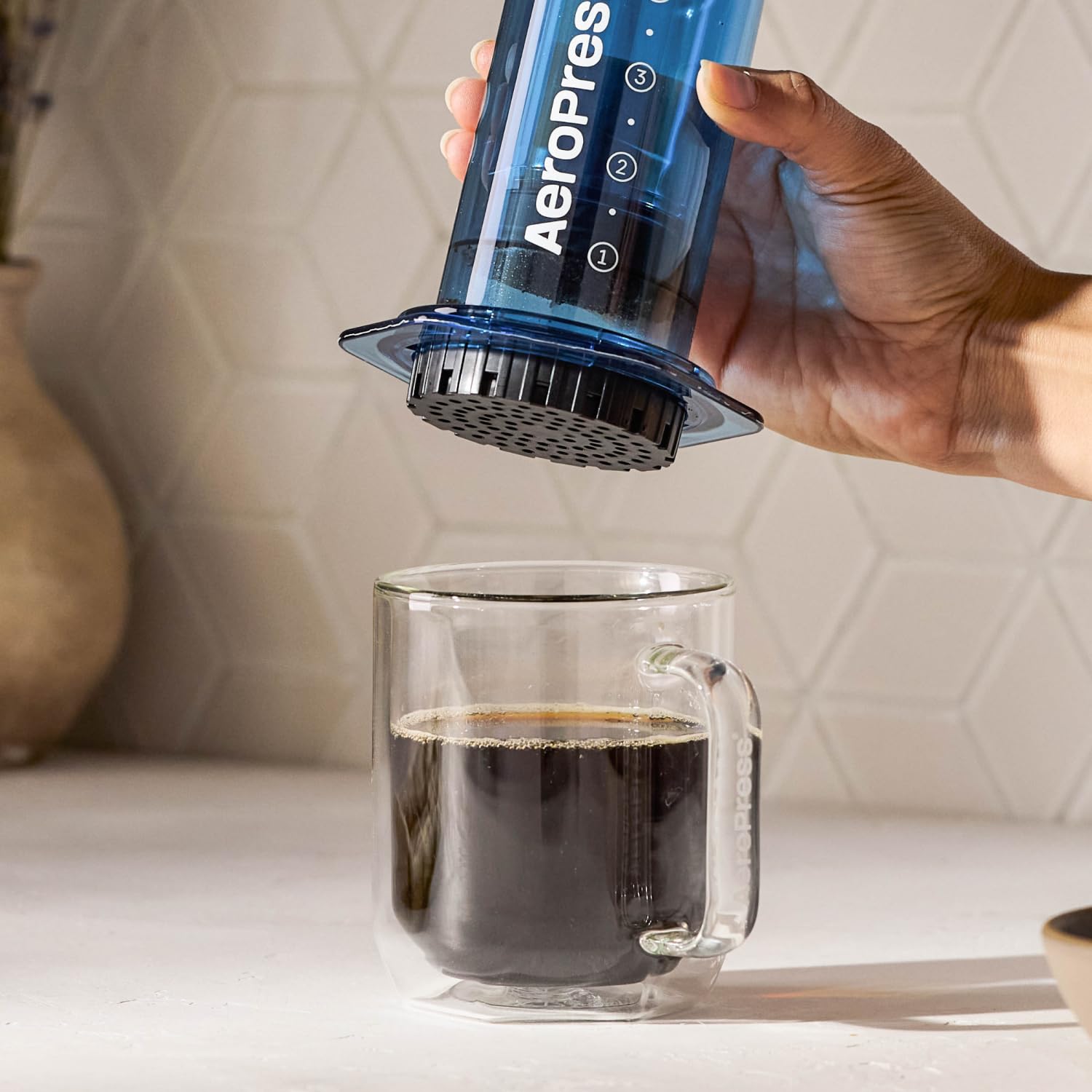 AeroPress clear blue next to a cup for scale showing portable travel size
