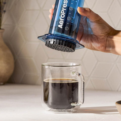 AeroPress clear blue next to a cup for scale showing portable travel size