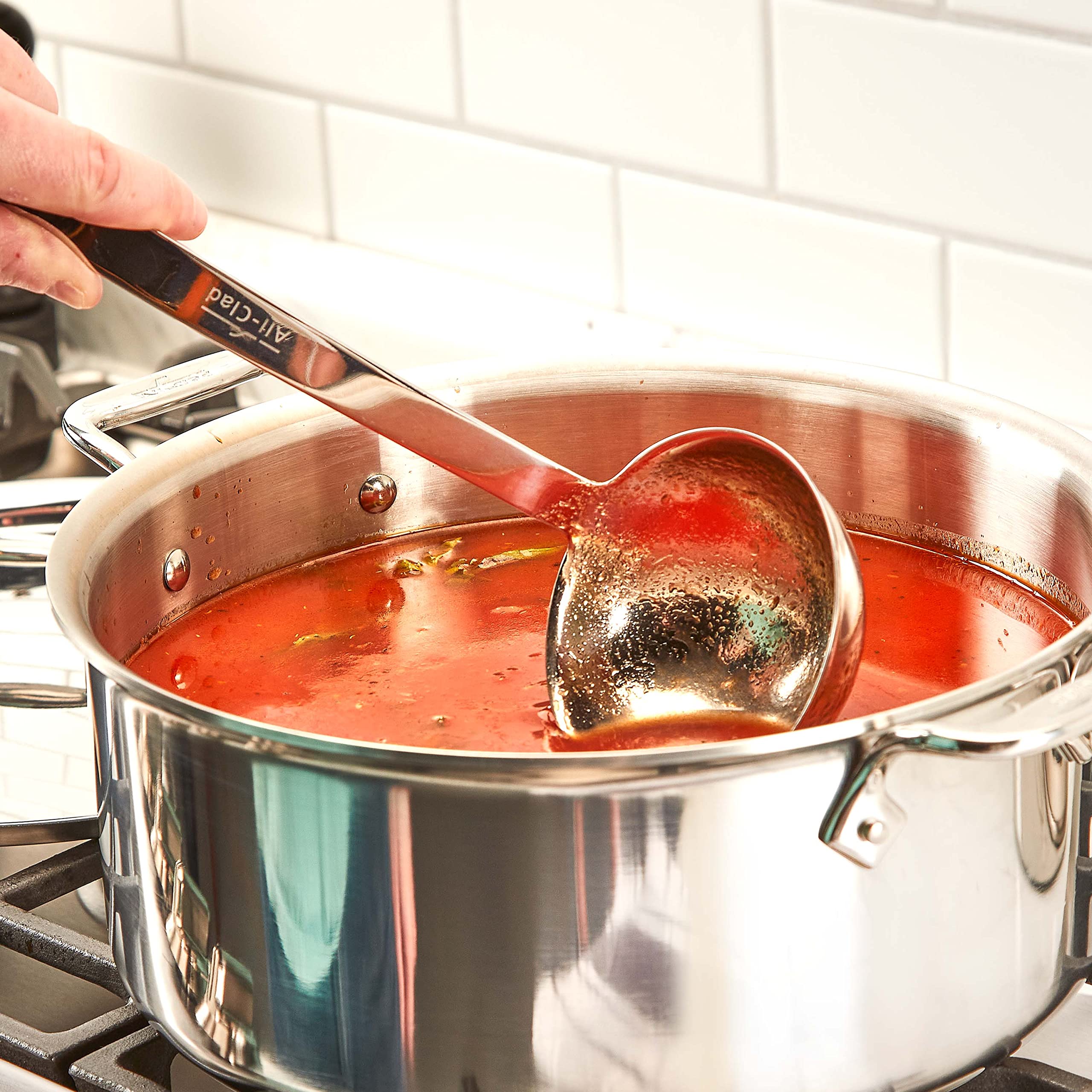 All-Clad ladle scooping soup from pot demonstrating balanced grip and drip-free pour
