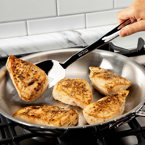 All-Clad turner in use on a grill demonstrating long reach and sturdy control for safe flipping