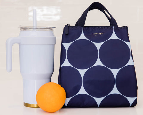 kate spade new york cooler beside a water bottle for scale showing compact capacity and travel friendliness