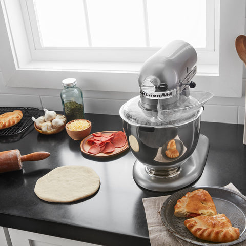 KitchenAid pouring shield beside stainless bowl to show size and fit compatibility