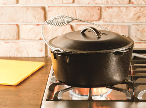Lodge Dutch oven with bail handle lifted over coals, safe outdoor cooking benefit